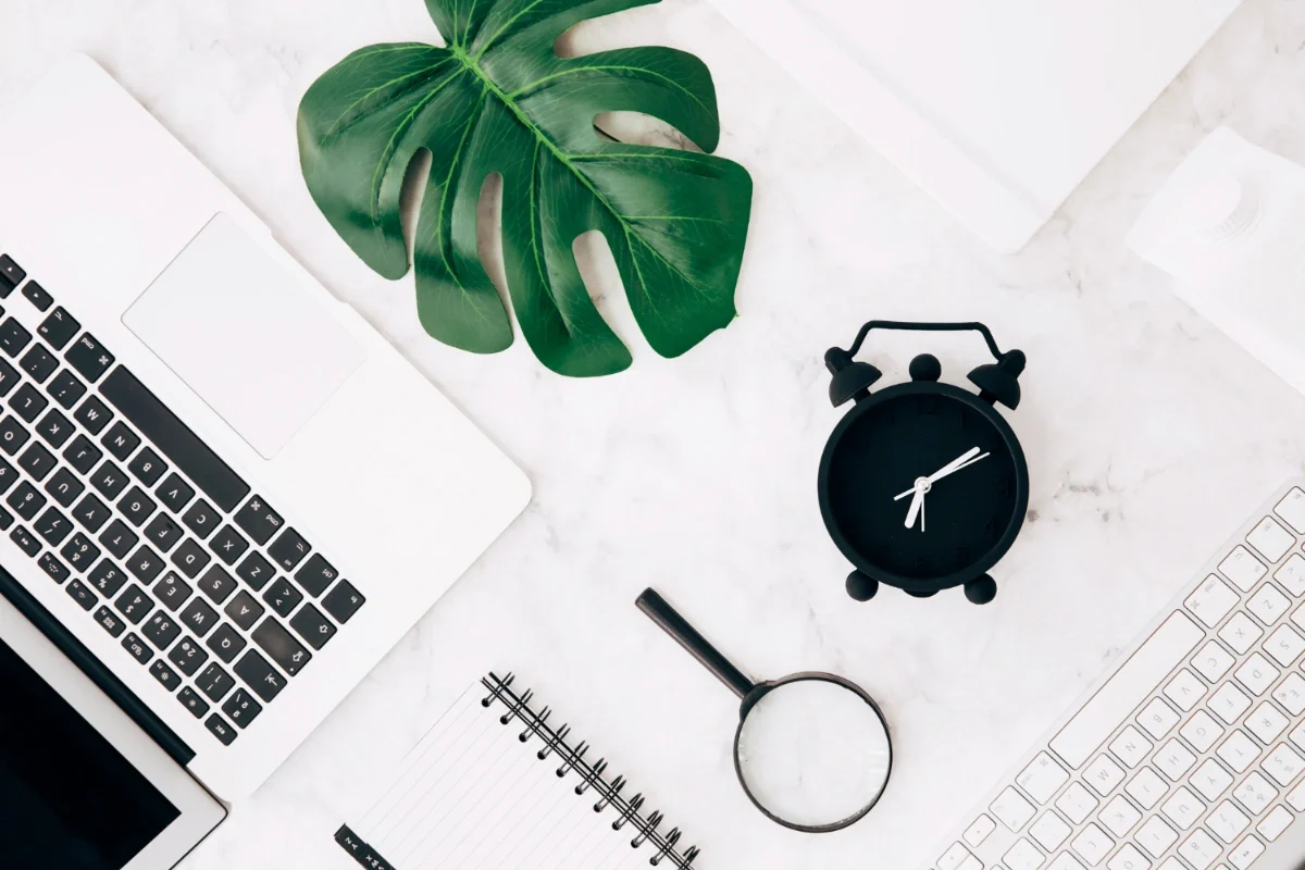 מחשב נייד עם שעון, זכוכית מגדלת ועלה ליד